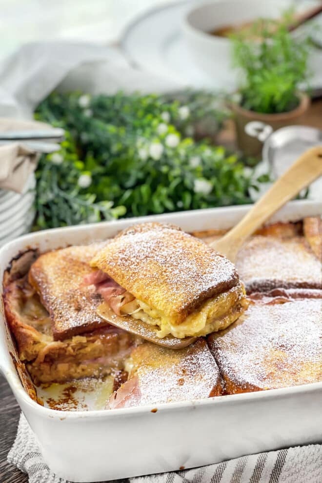 Monte Cristo casserole in a white baking dish, spatula lifting a serving out.