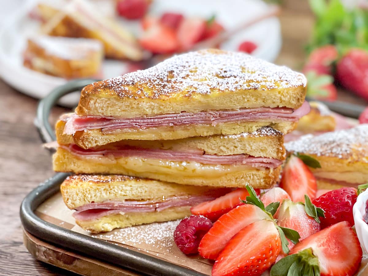 Monte Cristo sandwiches cut diagonally, stacked, and dusted with powdered sugar. Strawberries on the side.