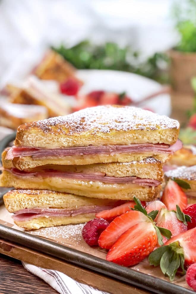 Monte Cristo sandwiches cut diagonally, stacked, and dusted with powdered sugar. Strawberries on the side.