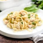 White plate of chicken fettuccine alfredo sprinkled with black pepper and fresh parsley.
