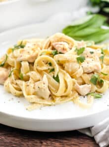 White plate of chicken fettuccine alfredo sprinkled with black pepper and fresh parsley.