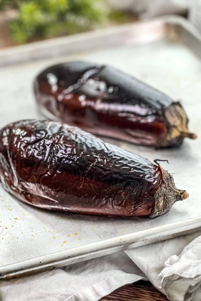 Two whole roasted eggplants on a baking sheet.
