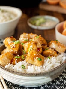 Chicken pieces in orange sauce on rice, topped with sesame seeds and green onion.