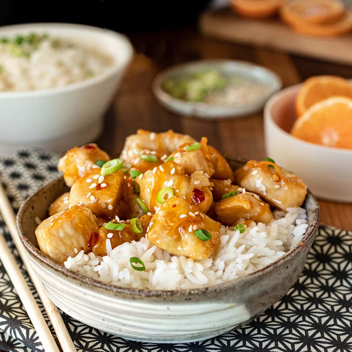 Chicken pieces in orange sauce on rice, topped with sesame seeds and green onion.