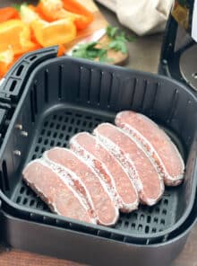 Five frozen Italian sausages together in an air fryer basket.