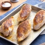 Four juicy, browned chicken breasts on a baking sheet.