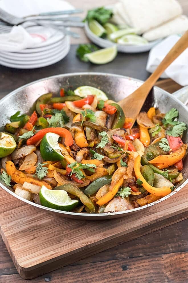 Skillet with fajita veggies and lime wedges.