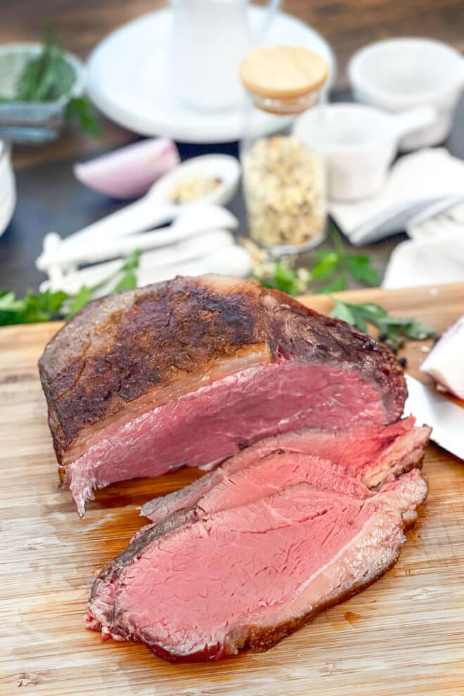 Roast beef with slices cut on a wooden cutting board.
