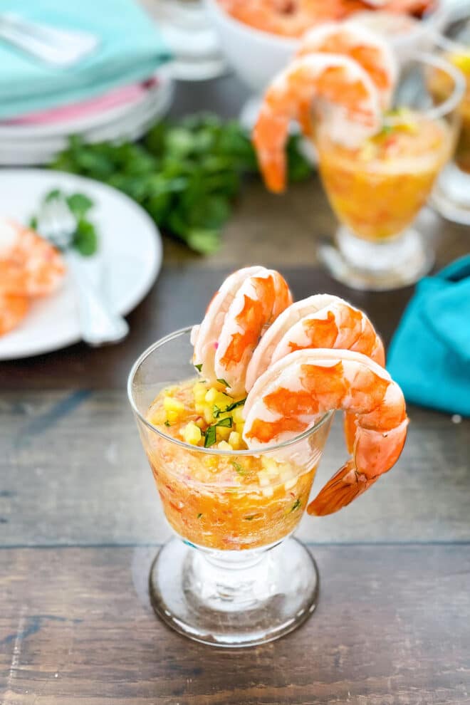 Glass with tropical cocktail sauce with chopped pineapple, shrimp hanging off the side.