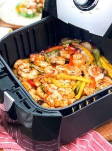 Air fryer with shrimp and fajita veggies in the basket.