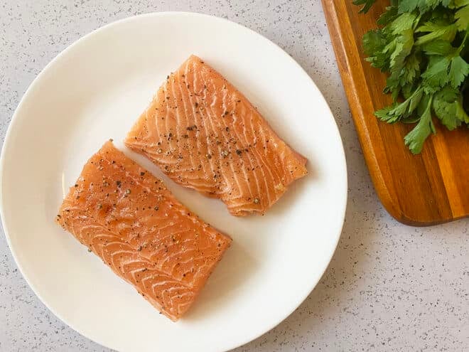 Two pieces of salmon seasoned with salt and pepper on a white plate