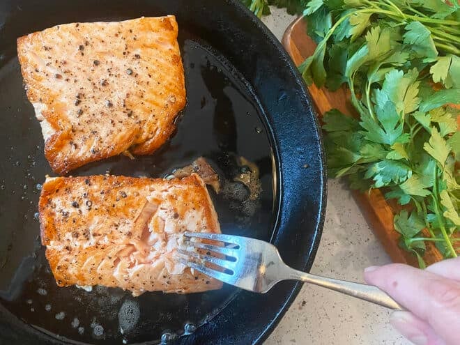 Salmon in a cast iron skillet, checking doneness with fork.