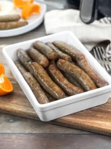 Breakfast sausage links on a white platter, with eggs and oranges in background.
