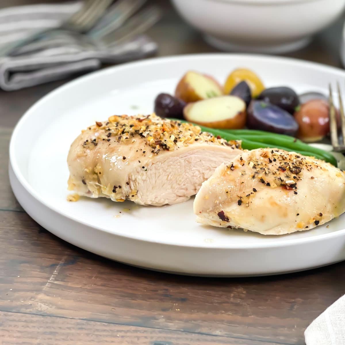 Seasoned baked chicken breast cut in half on a white plate with green beans and potatoes.
