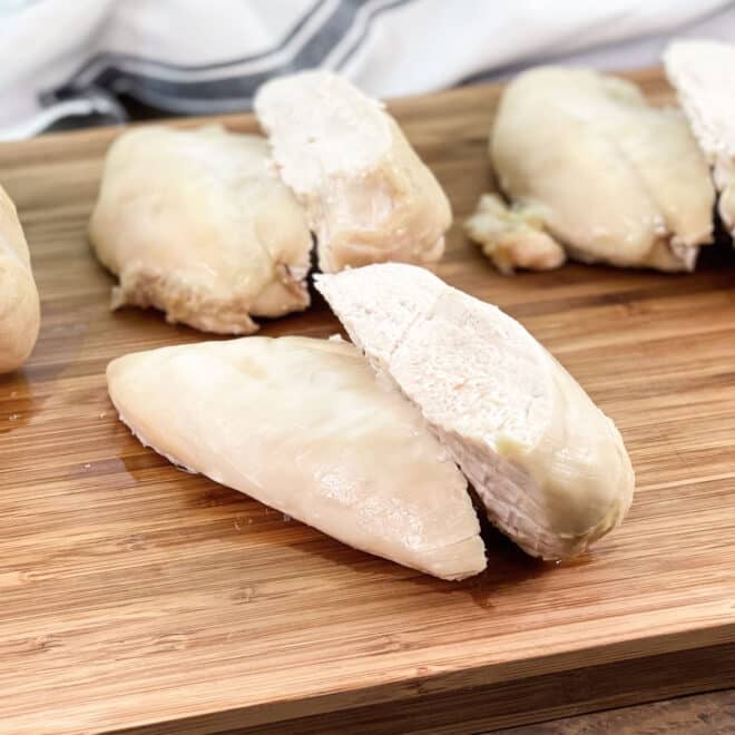 Halved cooked chicken breast on wooden cutting board.