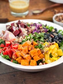 White bowl with a rainbow salad - bell pepper, sweet potato, tomatoes and more over kale.