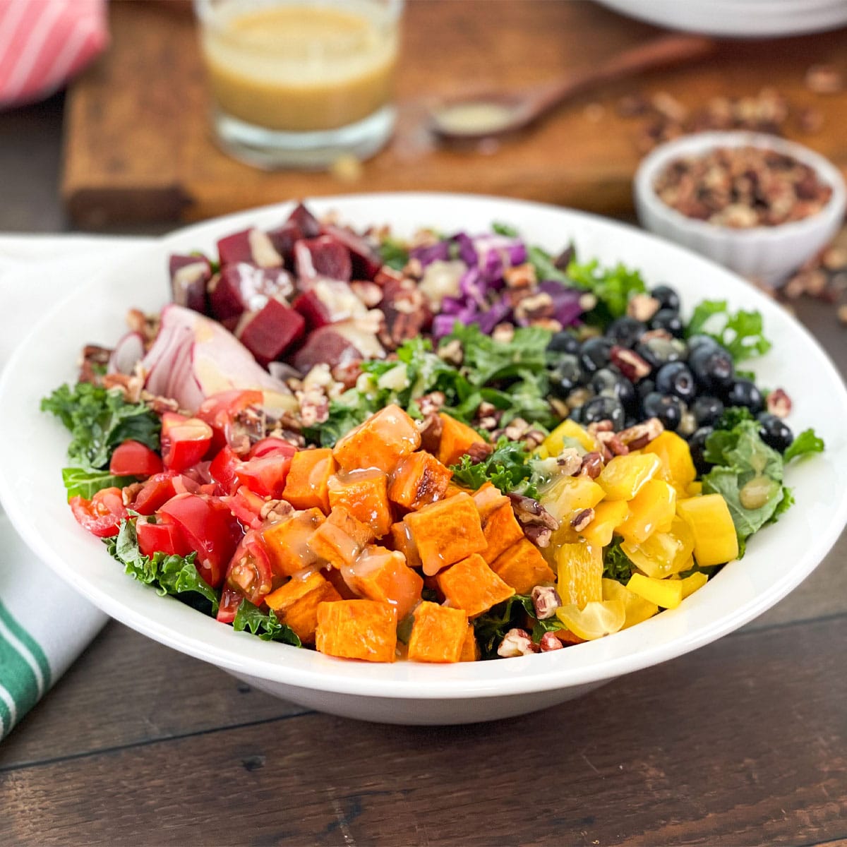 White bowl with a rainbow salad - bell pepper, sweet potato, tomatoes and more over kale.