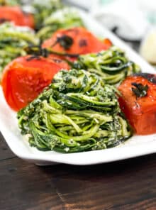 Piles of zoodles with pesto and whole grilled tomatoes on a white platter.