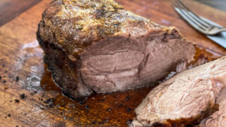 Pork butt roast on a wooden cutting board with several slices cut.