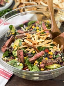 Glass bowl of steak salad with black beans, corn, avocado, and tortilla strips.