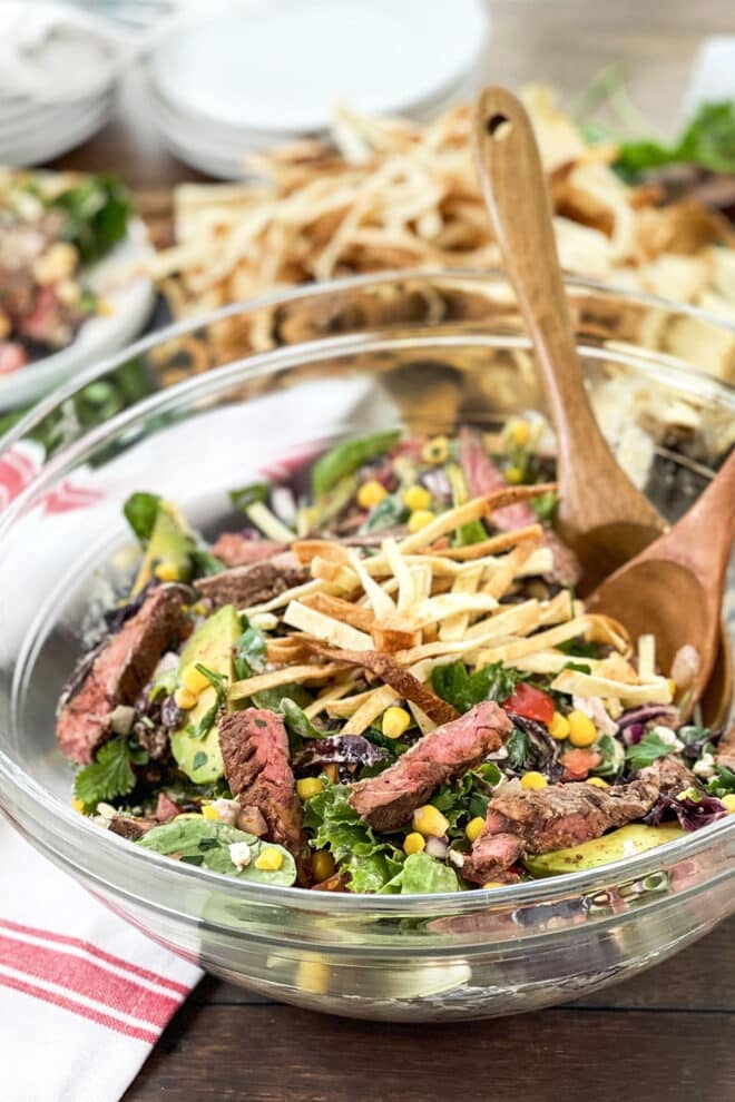 Glass bowl of steak salad with black beans, corn, avocado, and tortilla strips.