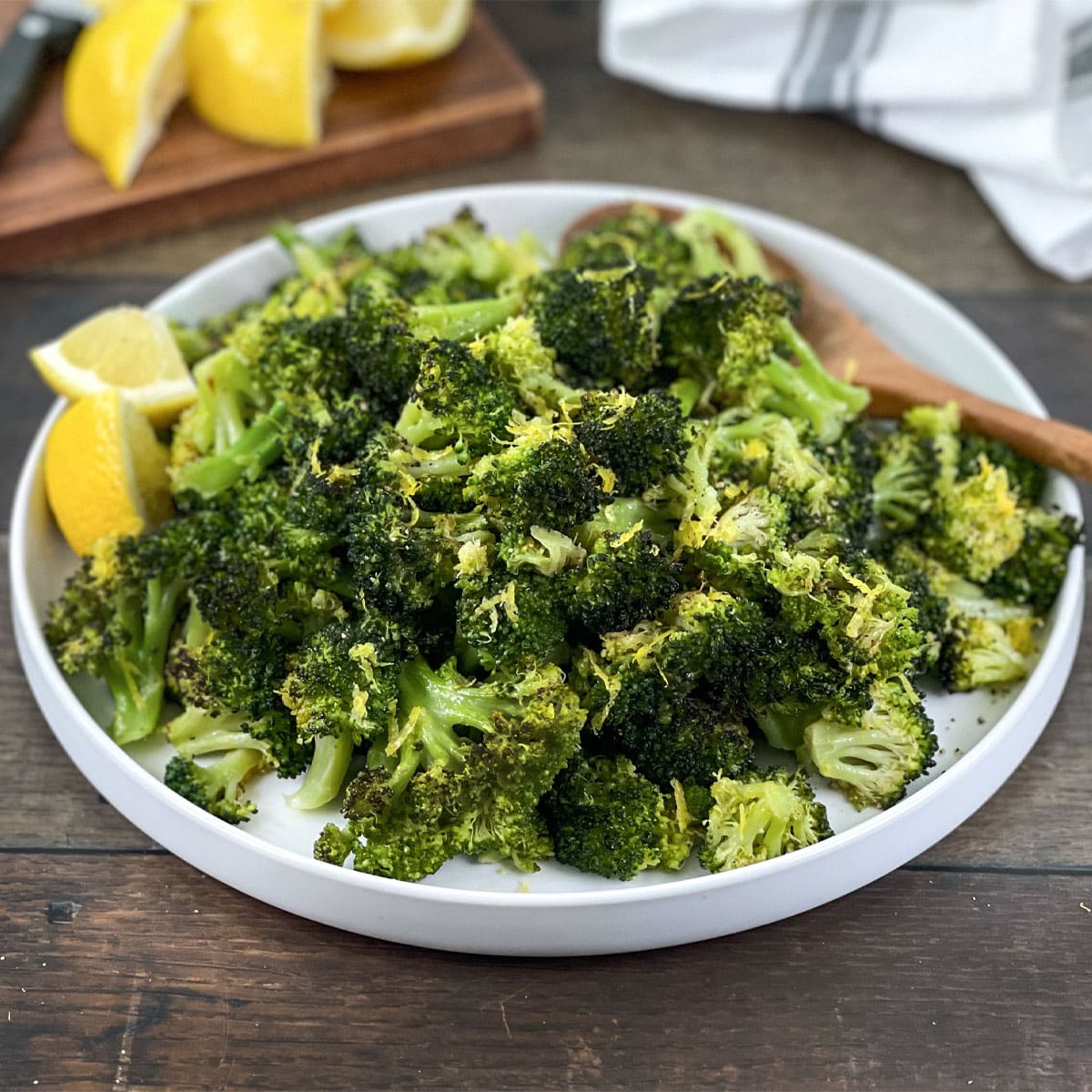 Cooked lemon butter broccoli florets on a white platter with lemon wedges.