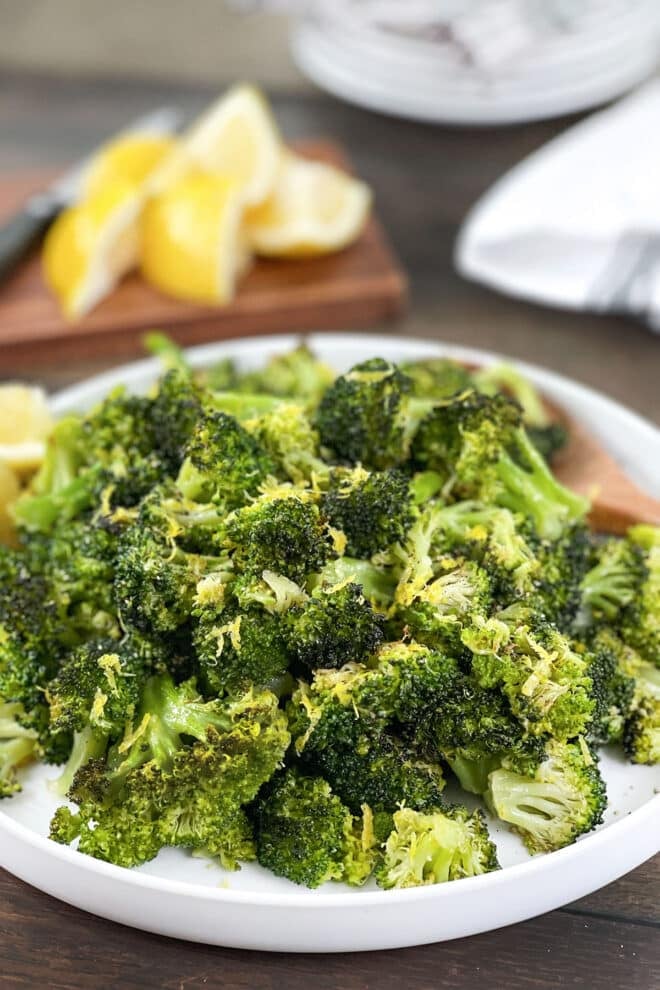 Cooked lemon butter broccoli florets on a white platter with lemon wedges.