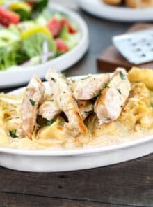 Tortelloni in alfredo sauce topped with cheese and slices of chicken.