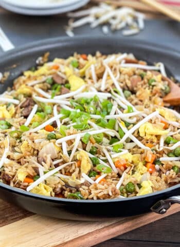 Skillet of pork fried rice topped with bean sprouts and green onion.