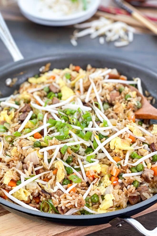 Skillet of pork fried rice topped with bean sprouts and green onion.