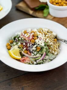 White bowl of quinoa salad with greens, onion, chickpeas, and lemon.