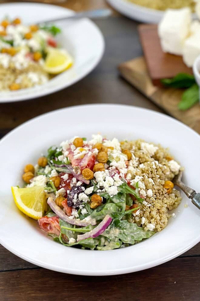 White bowl of quinoa salad with greens, onion, chickpeas, and lemon.