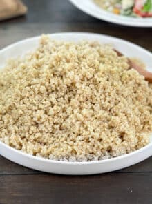White dish of cooked quinoa and wooden spoon.