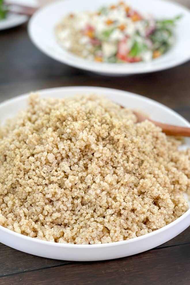 White dish of cooked quinoa and wooden spoon.