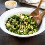 broccoli salad with cashews in a white bowl with wooden spoons