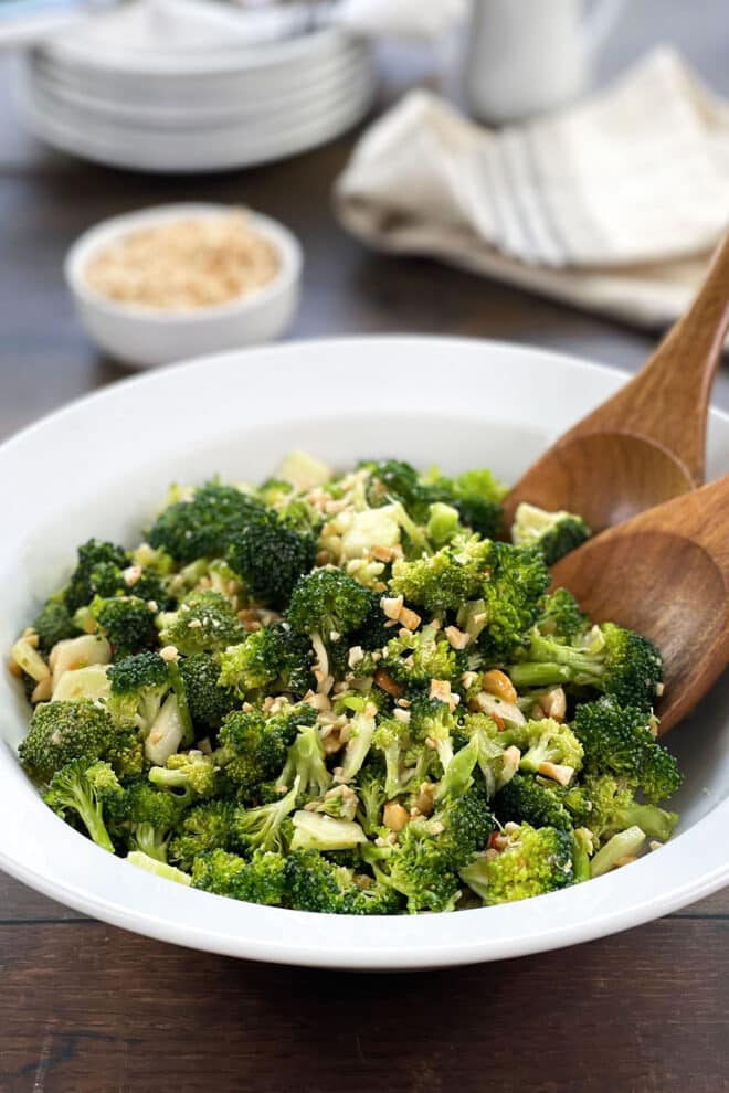 broccoli salad with cashews in a white bowl with wooden spoons