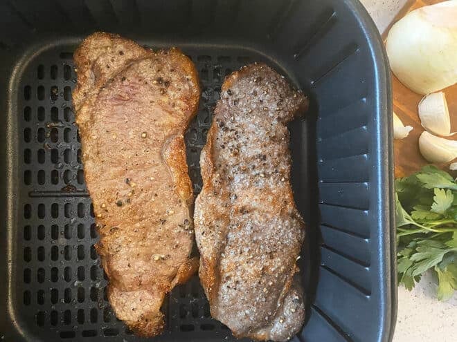 Cooked steaks in an air fryer basket.