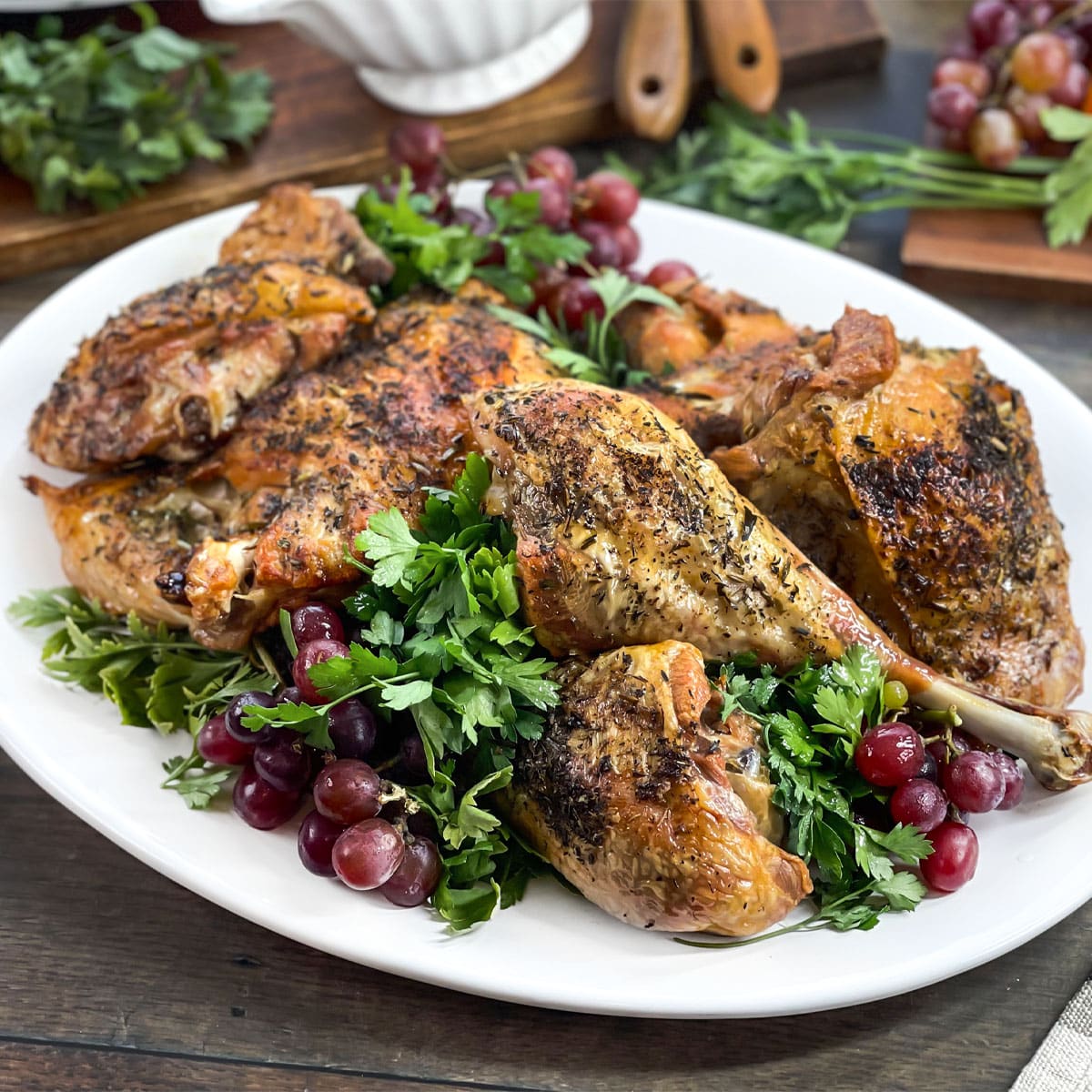 Roasted turkey pieces on a white platter with greens and grapes.