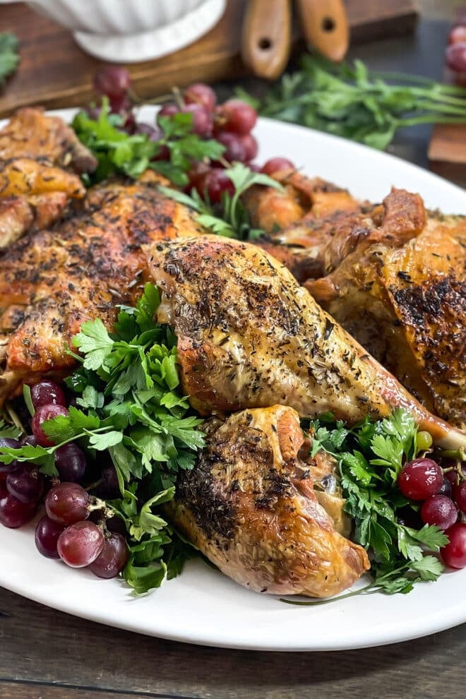 Roasted turkey pieces on a white platter with greens and grapes.