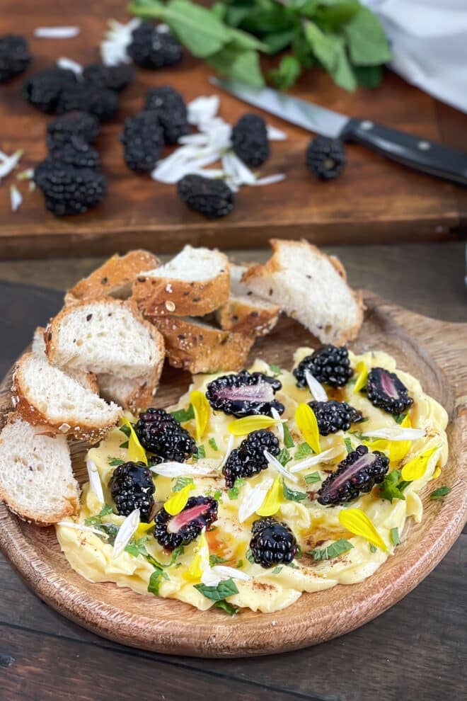 Round butter board with blackberries, mint, and honey with fresh bread on board.