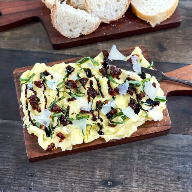 Butter spread on wooden board topped with balsamic and parmesan.