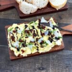Butter board with balsamic glaze, fresh basil, and shaved Parmesan with bread in background.