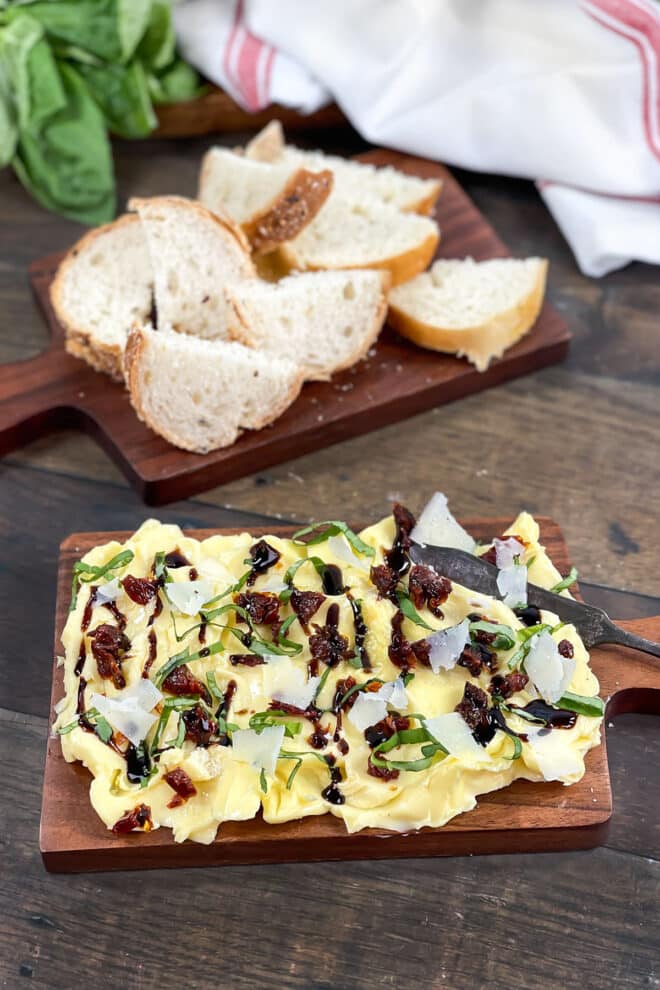 Butter board with balsamic glaze, fresh basil, and shaved Parmesan with bread in background.