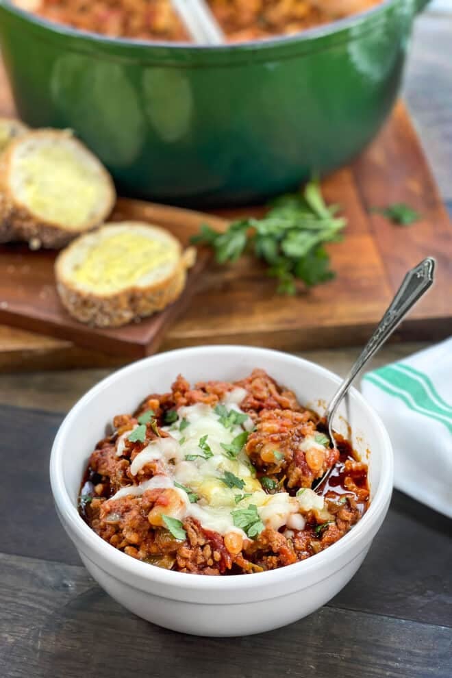 White bowl of sausage chili topped with melted Italian cheese.