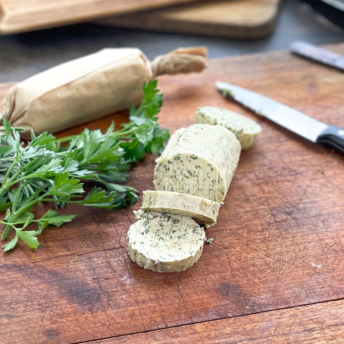 Log of compound butter for turkey on a wooden cutting board next to fresh parsley.