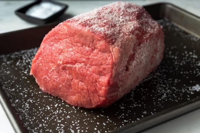 A beef roast coated in salt on a sheet pan. This is dry-brining a roast beef.
