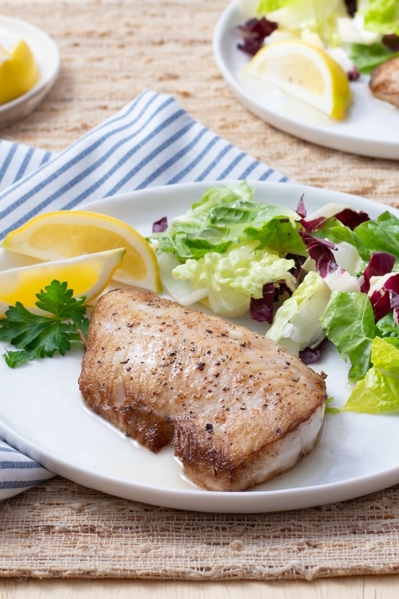 Cooked fish fillet on a plate with salad and lemon wedges.