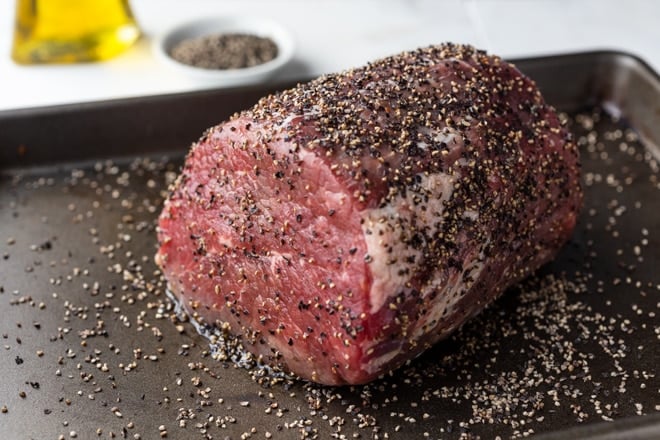 An uncooked beef roast on a pan coated with black pepper.