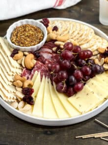 Charcuterie board with cheese, meat, crackers, grapes, and nuts.