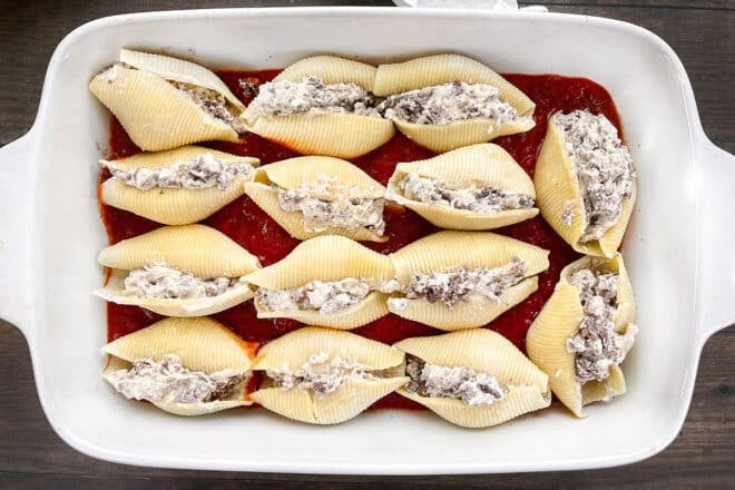 Jumbo shells stuffed with ricotta and ground beef in a casserole dish with tomato sauce.